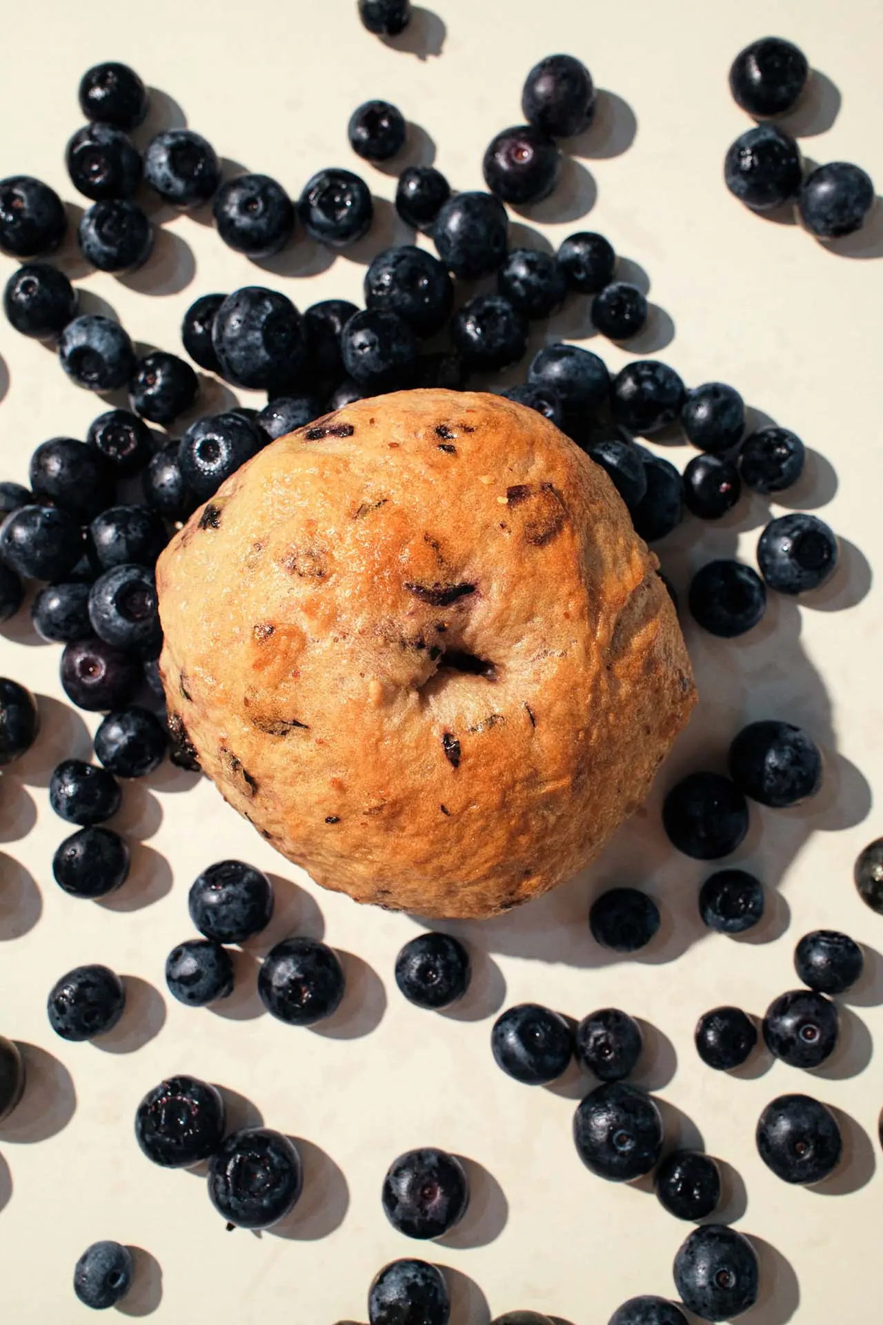 A blueberry bagel studded with dark berries, surrounded by fresh blueberries.