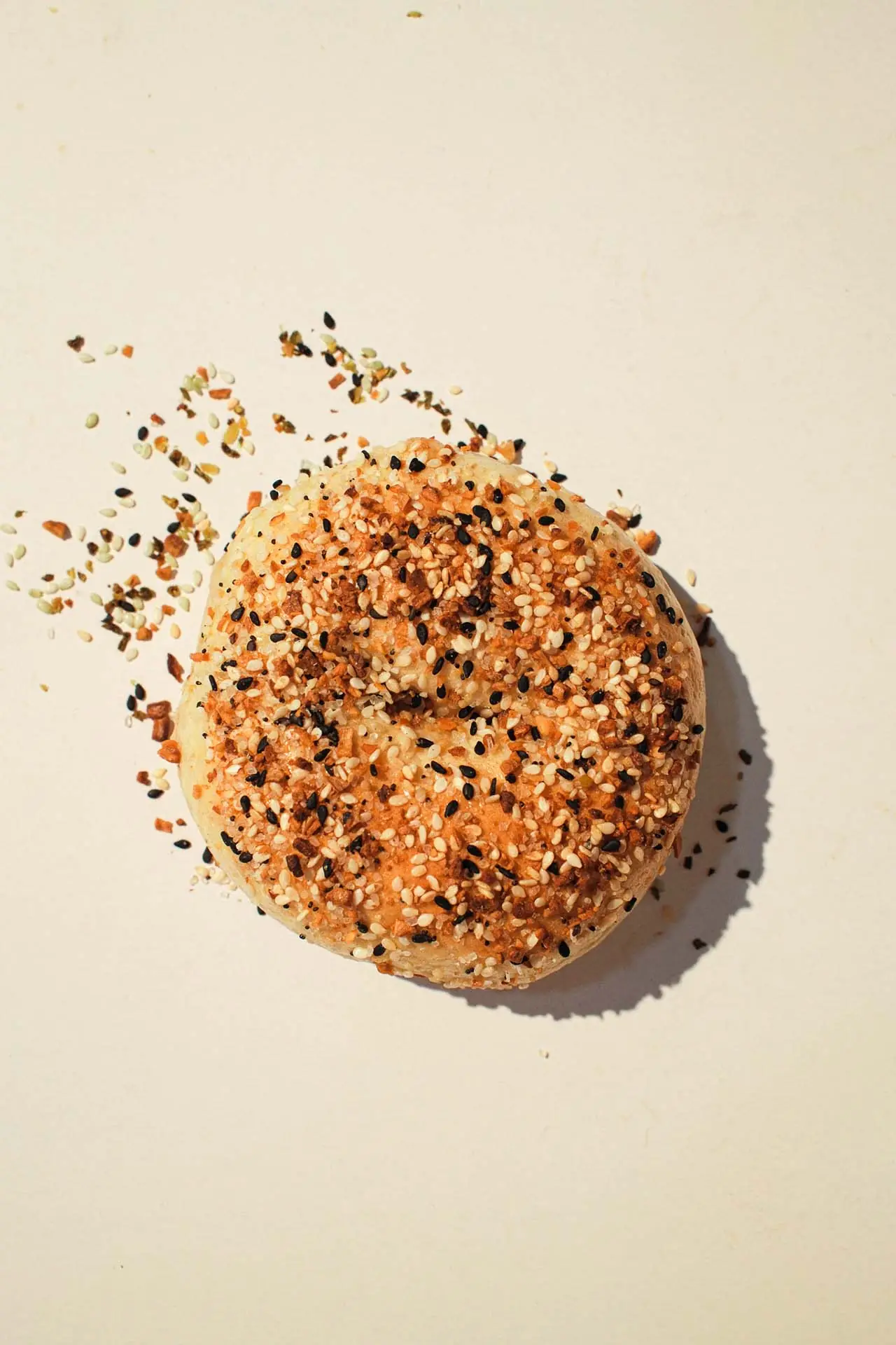 An everything bagel topped with sesame, poppy seeds, garlic and onion, seeds scattered around it.