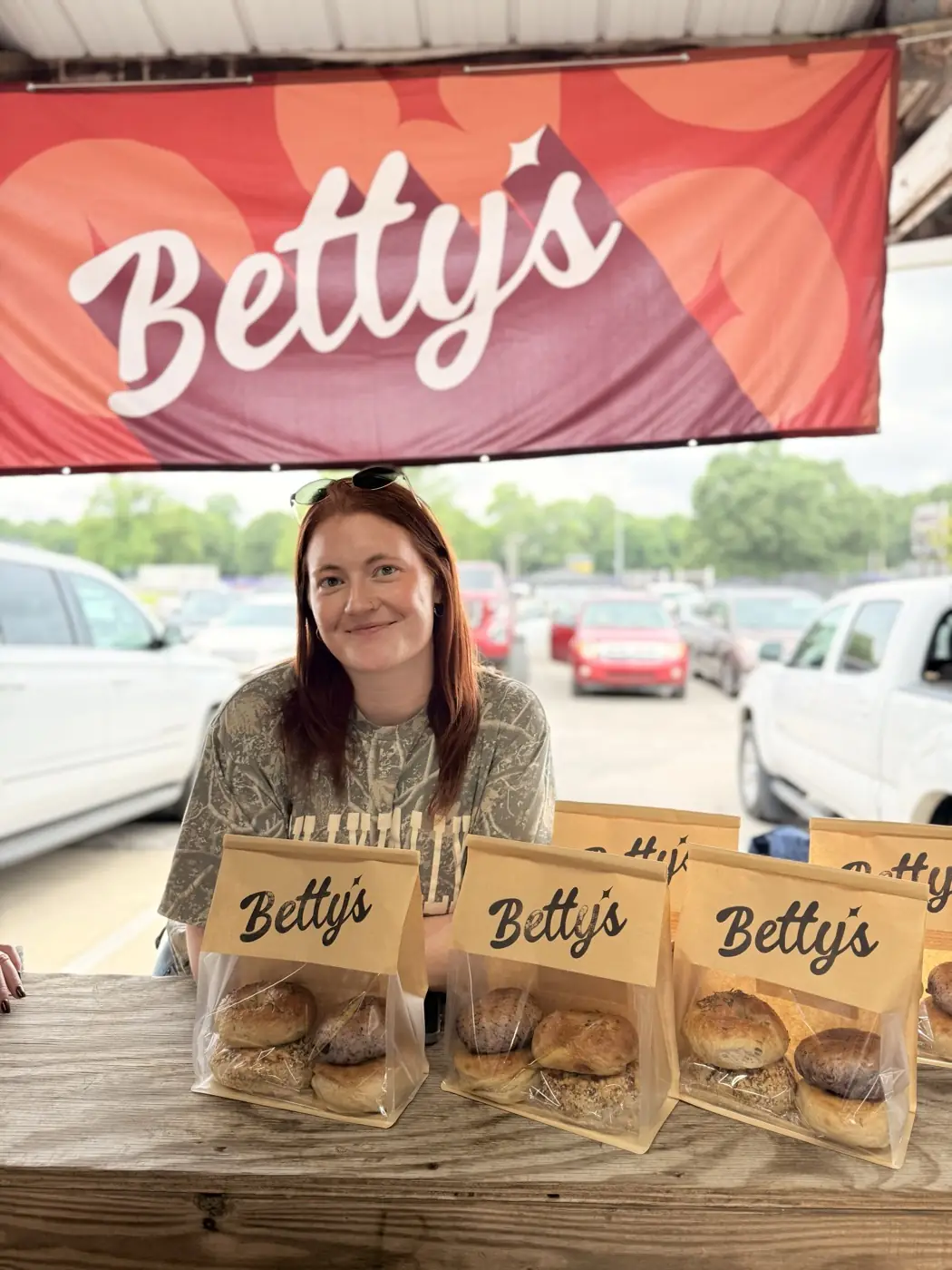 Betty behind the stall at the Florence Farmers Market, bagged bagels lined up on the table beneath the Betty's banner.