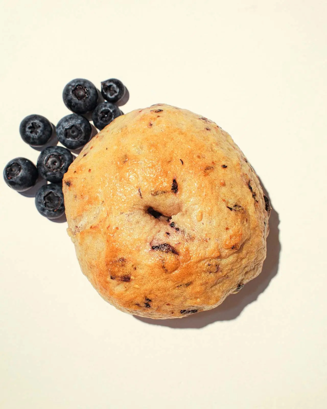 A blueberry bagel surrounded by fresh blueberries.