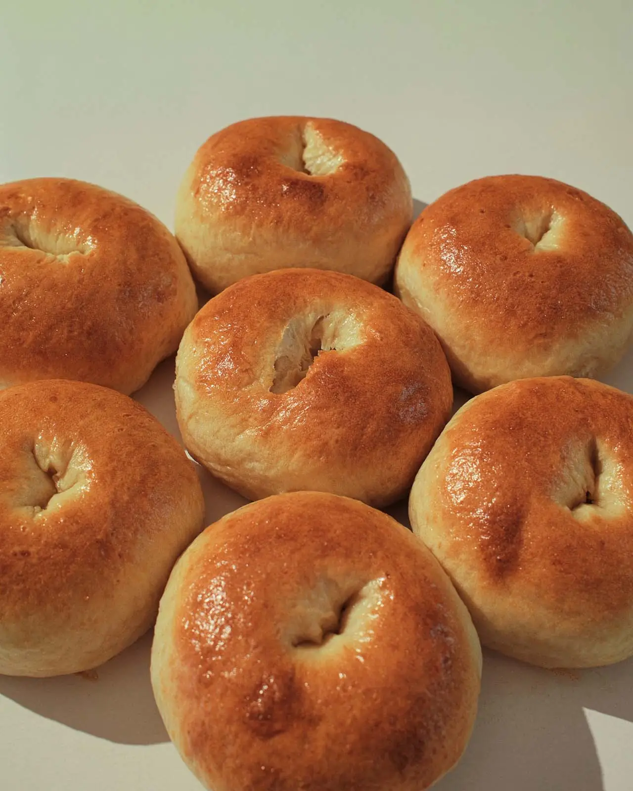 Golden plain bagels scattered across a cream surface.